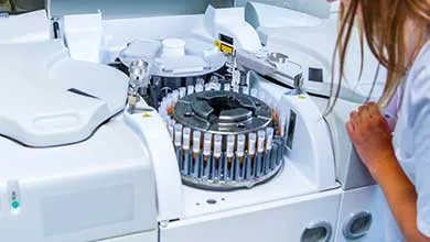 Lab technician monitoring a medical analyzer processing test tubes in a rotating carousel.