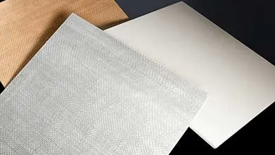 Close-up of three material samples fanned out on a dark background: a silvery-white sheet with a honeycomb texture, a tan woven sheet, and a smooth off-white sheet.