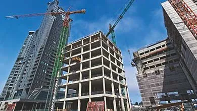 Low-angle view of multiple skyscrapers under construction, with large cranes set against a clear blue sky.