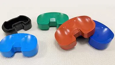 Five U-shaped plastic pieces in blue, green, black, and reddish-brown are arranged on a white surface.