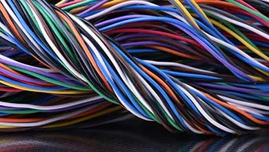 A thick, twisted bundle of multicolored wires lies on a dark, shiny surface.