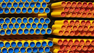 Stacks of yellow cylindrical pipes arranged horizontally, with bundles on the left showing bright blue ends and bundles on the right showing reddish-orange ends, all secured with black straps.