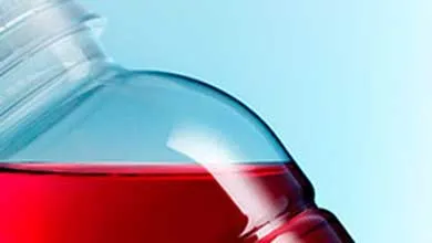 Close-up of a tilted bottle with red liquid, set against a light blue background.