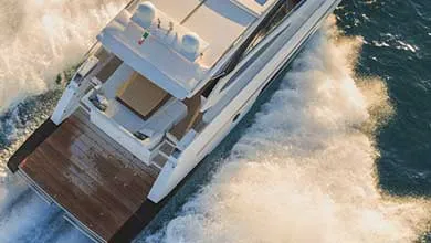 Aerial view of a white motor yacht moving at speed across open water, creating a foamy wake.