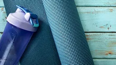 Reusable water bottle placed beside rolled exercise mats on a painted wooden surface.