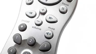Close-up of a silver remote control showing directional arrows, pause, volume up and down, mute buttons, and number keys 1 to 4.